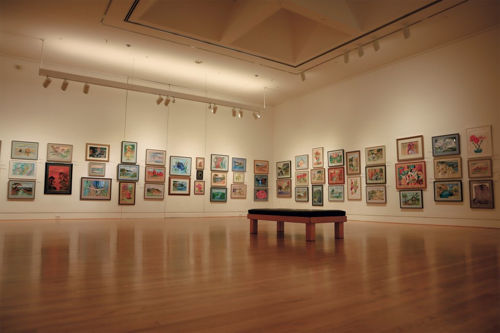 An art gallery with a wooden floor and a bench, displaying various colorful framed artworks on the walls in Santa Clara, California.