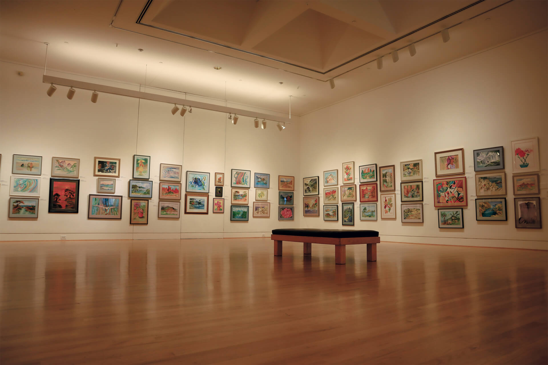 Museu de Arte Tritão An art gallery with a wooden floor and a bench, displaying various colorful framed artworks on the walls in Santa Clara, California.