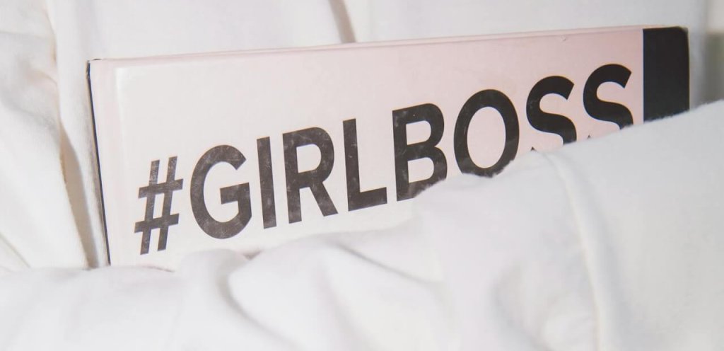 Close-up of a woman in white holding a #GirlBoss book, symbolizing empowerment and feminism.
