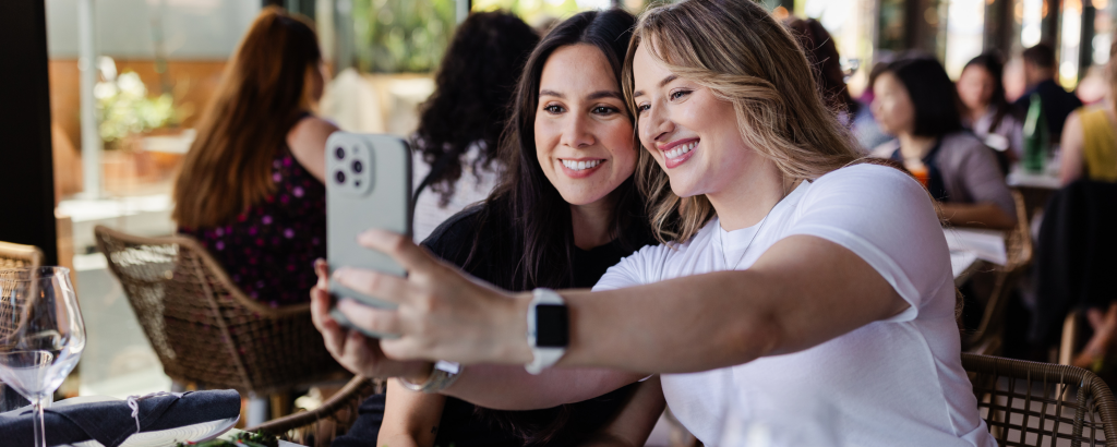 Two friends taking a selfie at a restaurant table in Santa Clara, California.