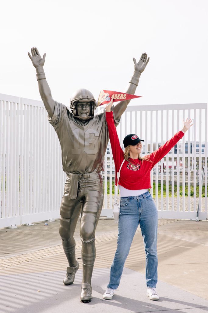Sports Tourism Woman in 49ers gear posing next to football player statue