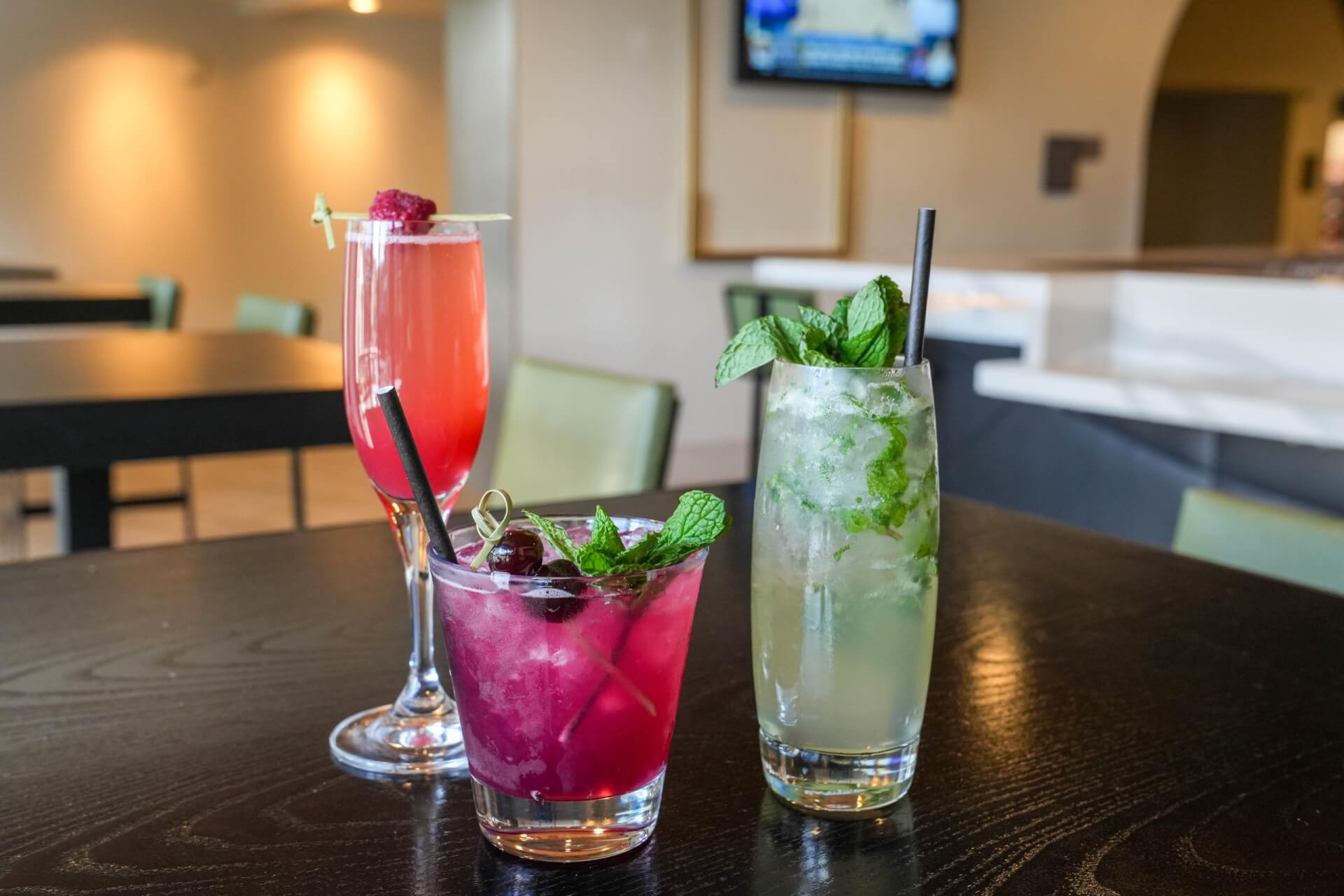 Three colorful cocktails on a table, garnished with fruits and herbs in Santa Clara, California.
