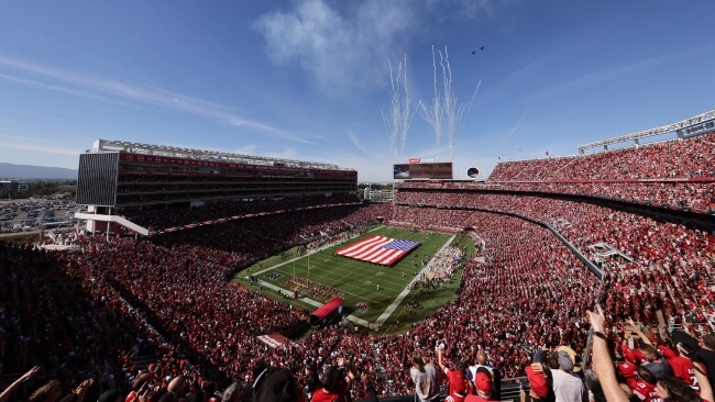 A vibrant football stadium filled with enthusiastic fans, featuring a prominent American flag and celebratory fireworks in Santa Clara, California.