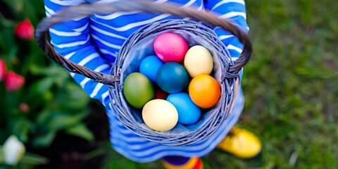 A child in a striped dress and yellow shoes holds a basket of colorful Easter eggs in Santa Clara, California.