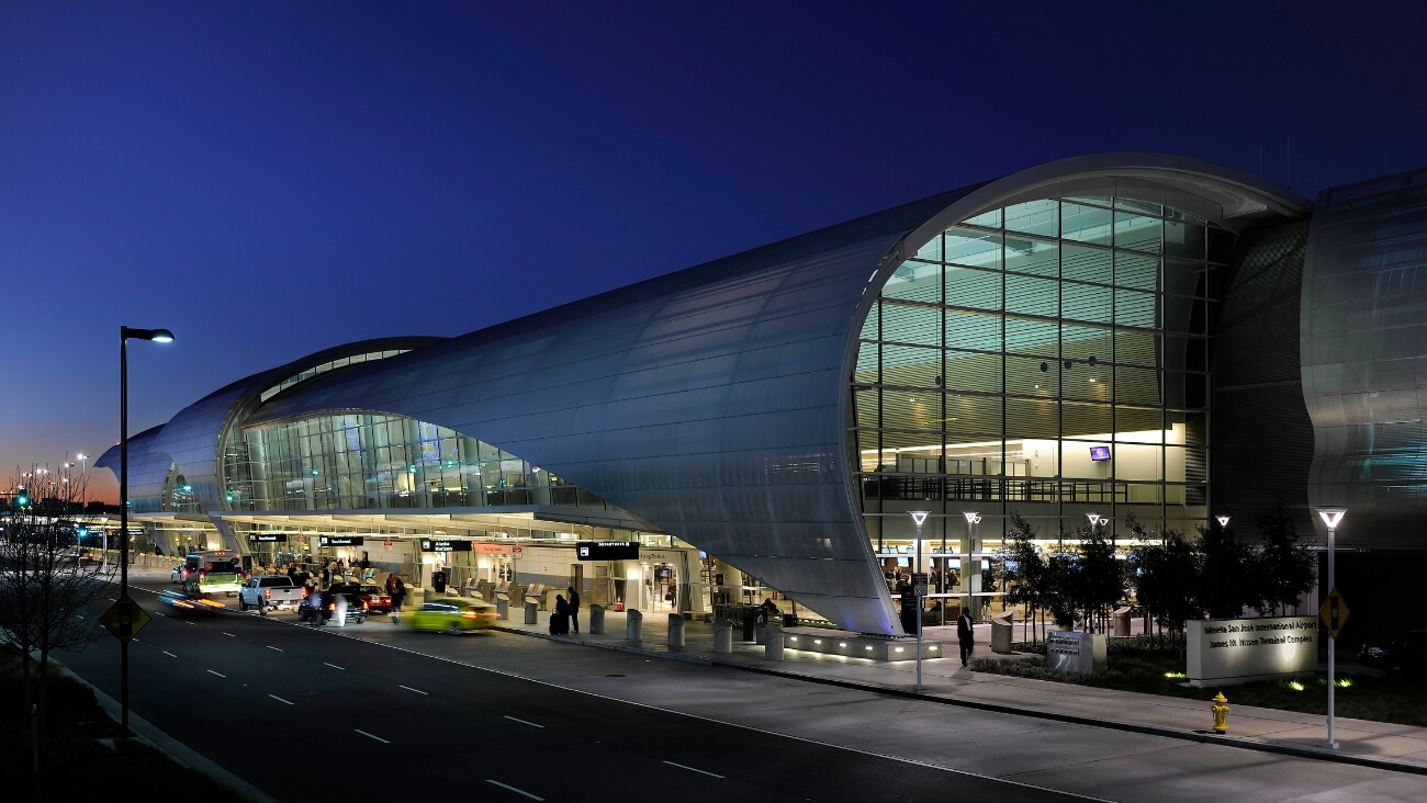 A modern airport terminal at dusk, featuring a distinctive curved glass facade in Santa Clara, California.