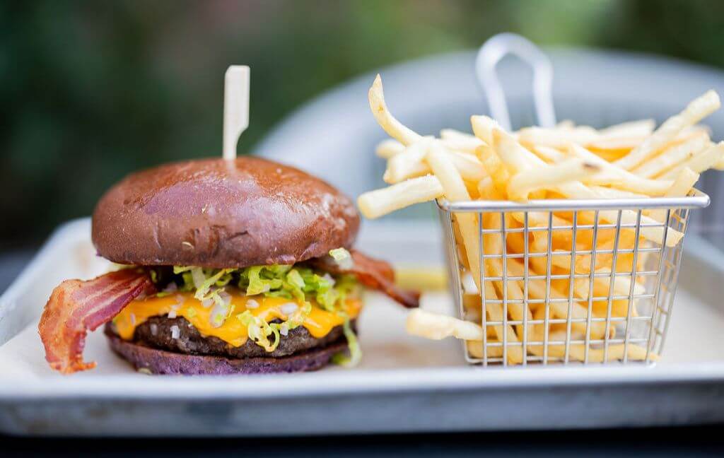 Food Trail 2026 A mouthwatering cheeseburger with bacon, lettuce, and tomato on a toasted bun, served with a side of crispy golden fries in a metal basket in Santa Clara, California.