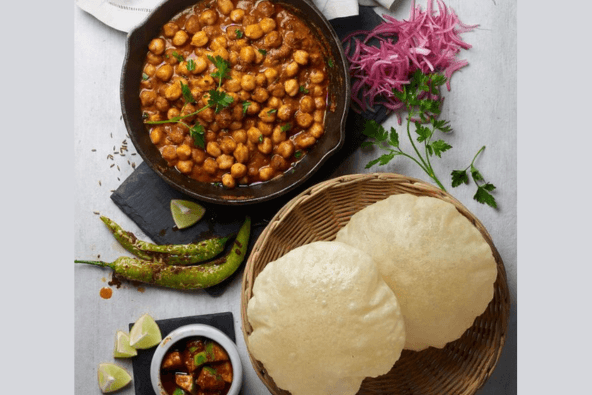 A traditional Indian meal featuring chickpea curry, puffy bread, and lime wedges in Santa Clara, California.