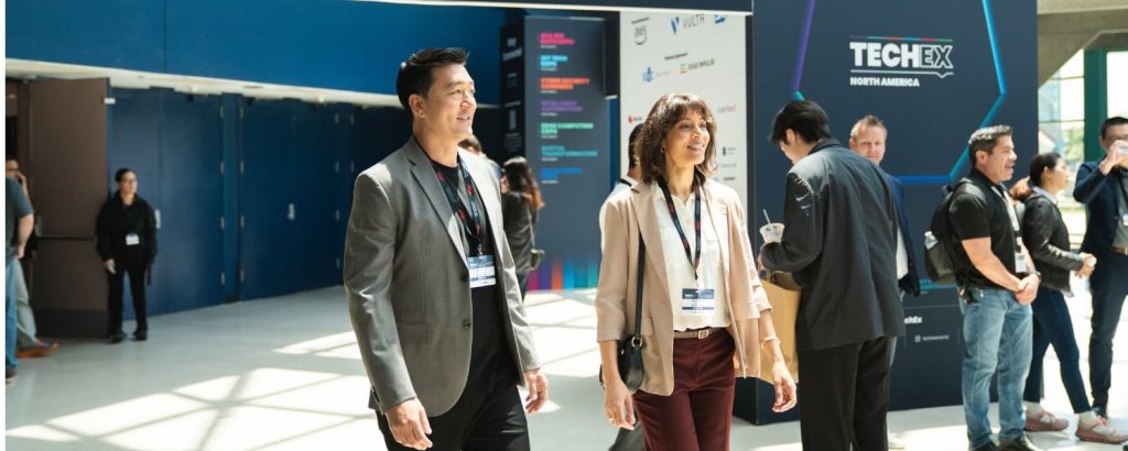 Attendees at a tech conference walk through a spacious lobby with banners and signs in Santa Clara, California.