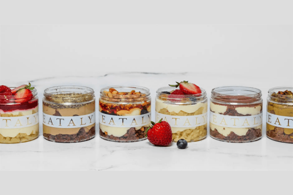 Six glass jars filled with colorful layers of desserts, topped with fresh fruits and nuts in Santa Clara, California.