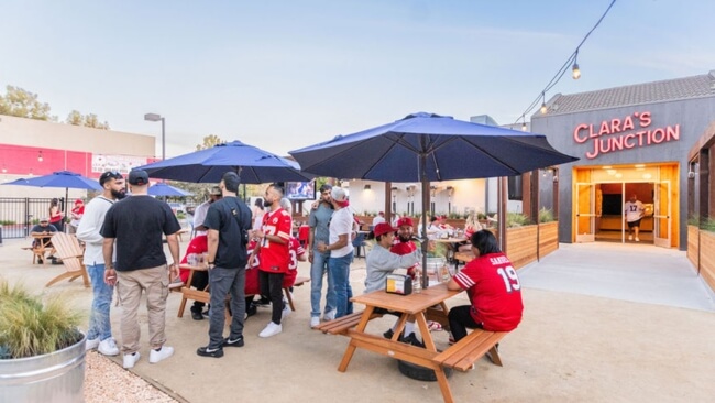 A group of people enjoying a casual outdoor gathering at Clara's Junction, with tables, umbrellas, and a relaxed atmosphere in Santa Clara, California.