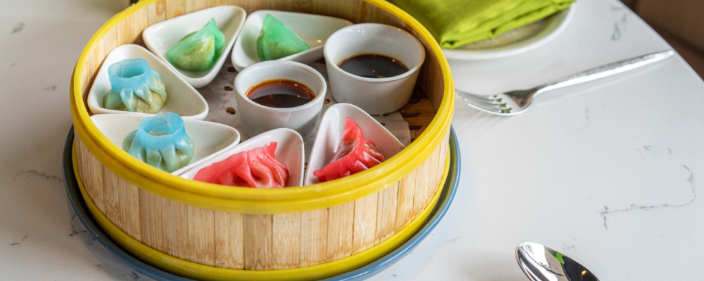 A colorful assortment of dim sum dumplings in a bamboo steamer basket, accompanied by dipping sauces in Santa Clara, California.