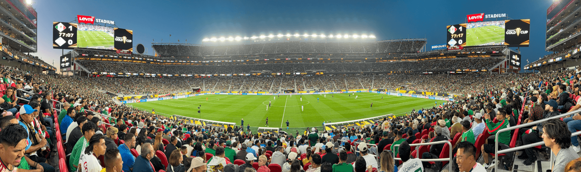 A panoramic view of a packed stadium during a soccer match, with bright lights illuminating the field and enthusiastic fans filling the stands in Santa Clara, California.