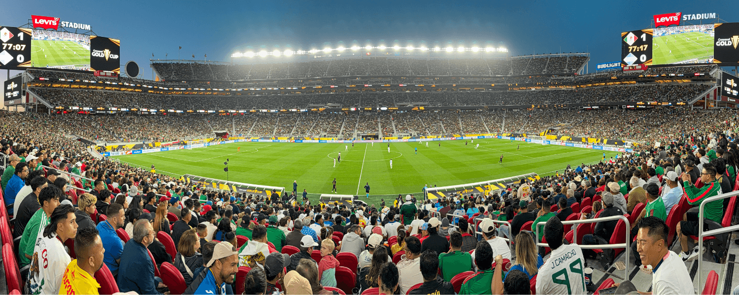 A panoramic view of a packed stadium during a soccer match, with bright lights illuminating the field and enthusiastic fans filling the stands in Santa Clara, California.