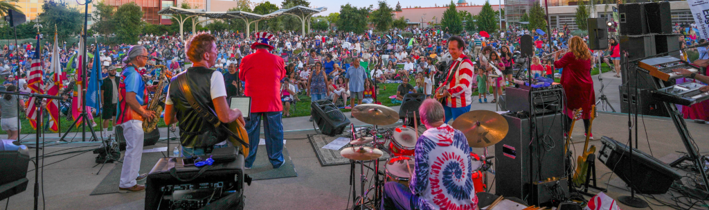 A vibrant outdoor concert with a large crowd enjoying live music in a park setting in Santa Clara, California.