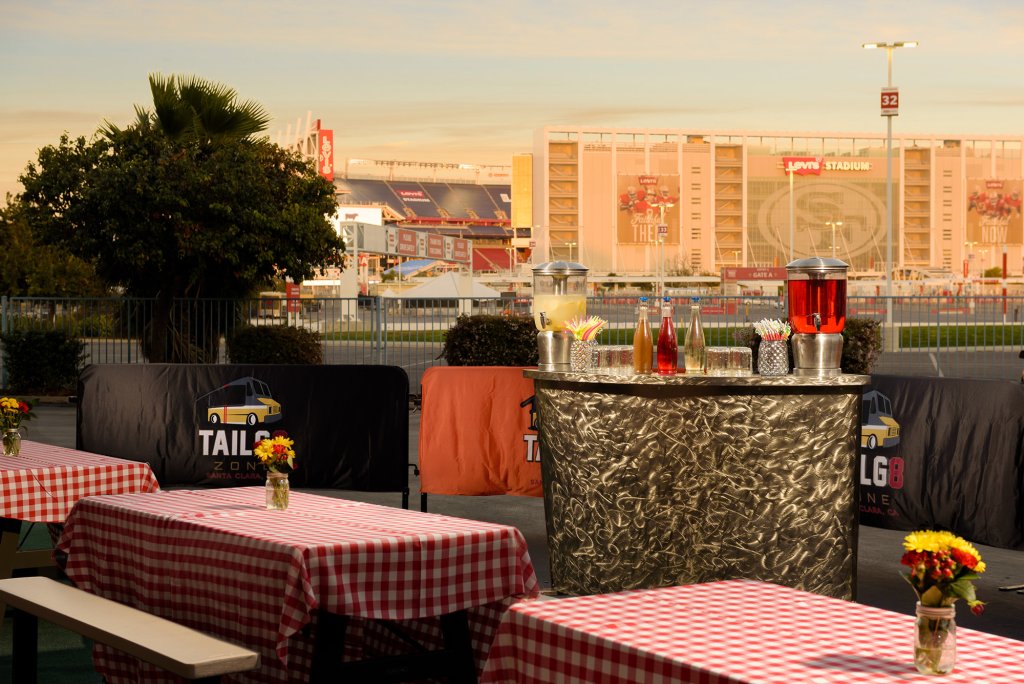 FIFA World Cup 2026 Outdoor event setup with picnic tables, checkered tablecloths, and a bar area near a stadium in Santa Clara, California.