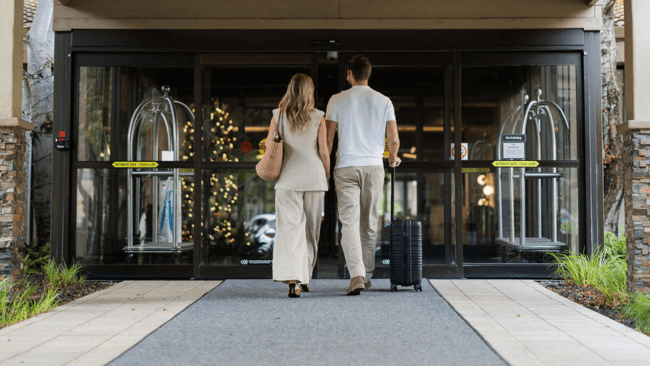 A couple walks hand in hand down a hotel driveway, pulling a suitcase behind them in Santa Clara, California.