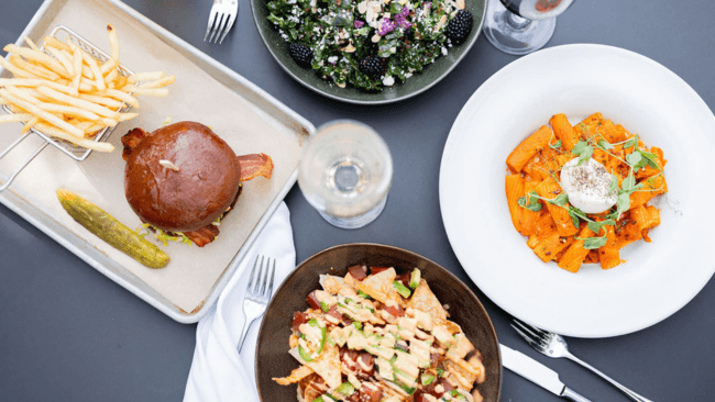 A variety of dishes including a burger with fries, a salad, pasta, and a bowl of nachos with avocado and chicken in Santa Clara, California.