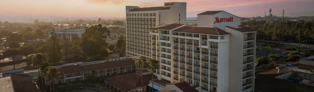 A panoramic view of a Marriott hotel complex with multiple buildings surrounded by lush greenery and palm trees at sunset in Santa Clara, California.