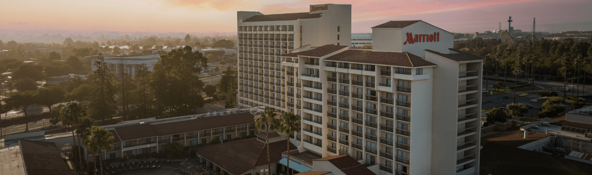 A panoramic view of a Marriott hotel complex with multiple buildings surrounded by lush greenery and palm trees at sunset in Santa Clara, California.