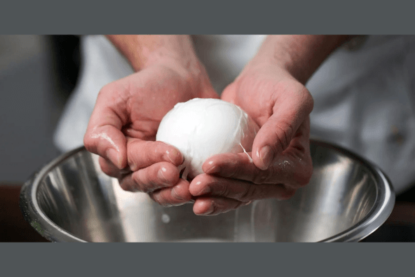 Hands-On: Mozzarella A chef gently cradles a perfectly poached egg in their hands over a stainless steel bowl in Santa Clara, California.