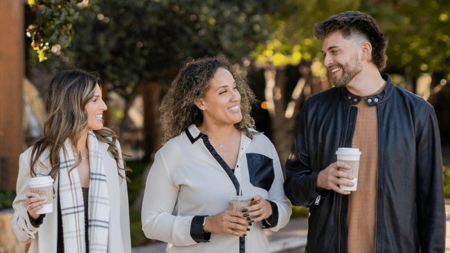 Three friends enjoying a sunny day outdoors, each holding a coffee cup and smiling in Santa Clara, California.