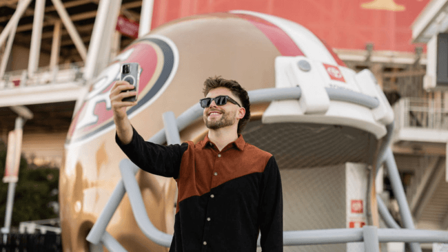 A man takes a selfie with a large 49ers helmet statue at a stadium in Santa Clara, California.