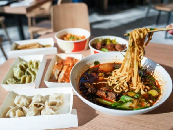 Bay Area Day Trips from Santa Clara: Itineraries for Every Schedule Chopsticks lifting noodles from a bowl of spicy beef noodle soup with side dishes in Santa Clara, California.