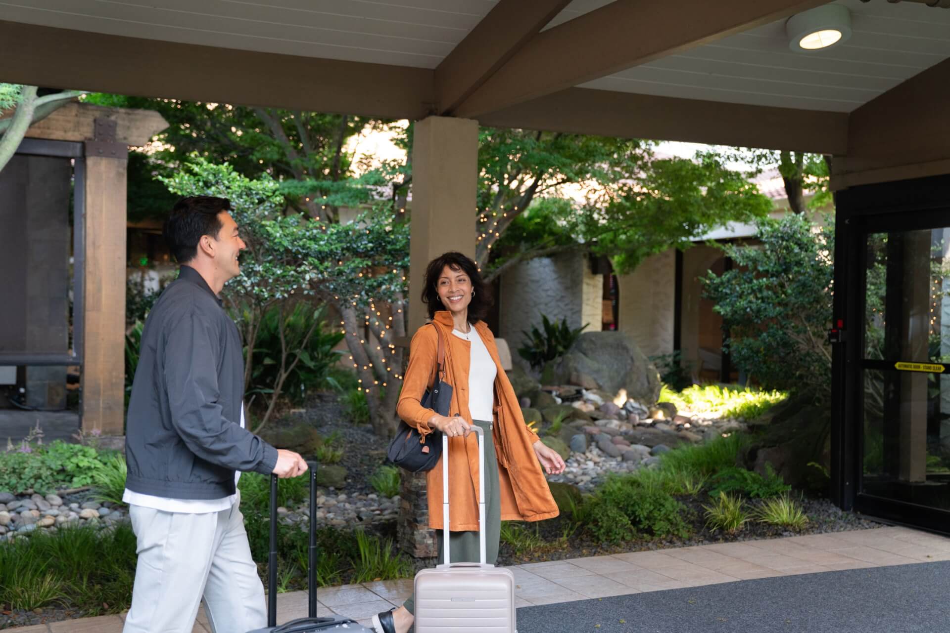 Bay Area Day Trips from Santa Clara: Itineraries for Every Schedule A man and a woman walking with luggage outside a building entrance in Santa Clara, California.