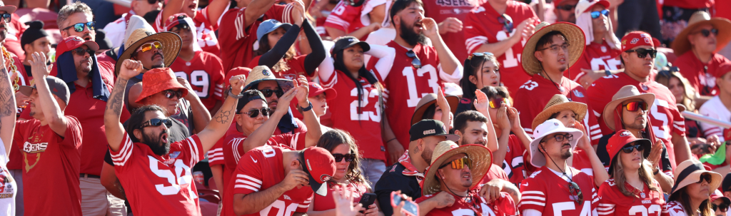 A crowd of fans wearing red San Francisco 49ers jerseys cheering at a stadium in Santa Clara, California.