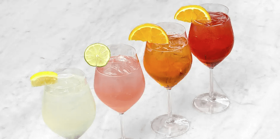 Four colorful cocktails in wine glasses garnished with citrus slices on a marble surface in Santa Clara, California.