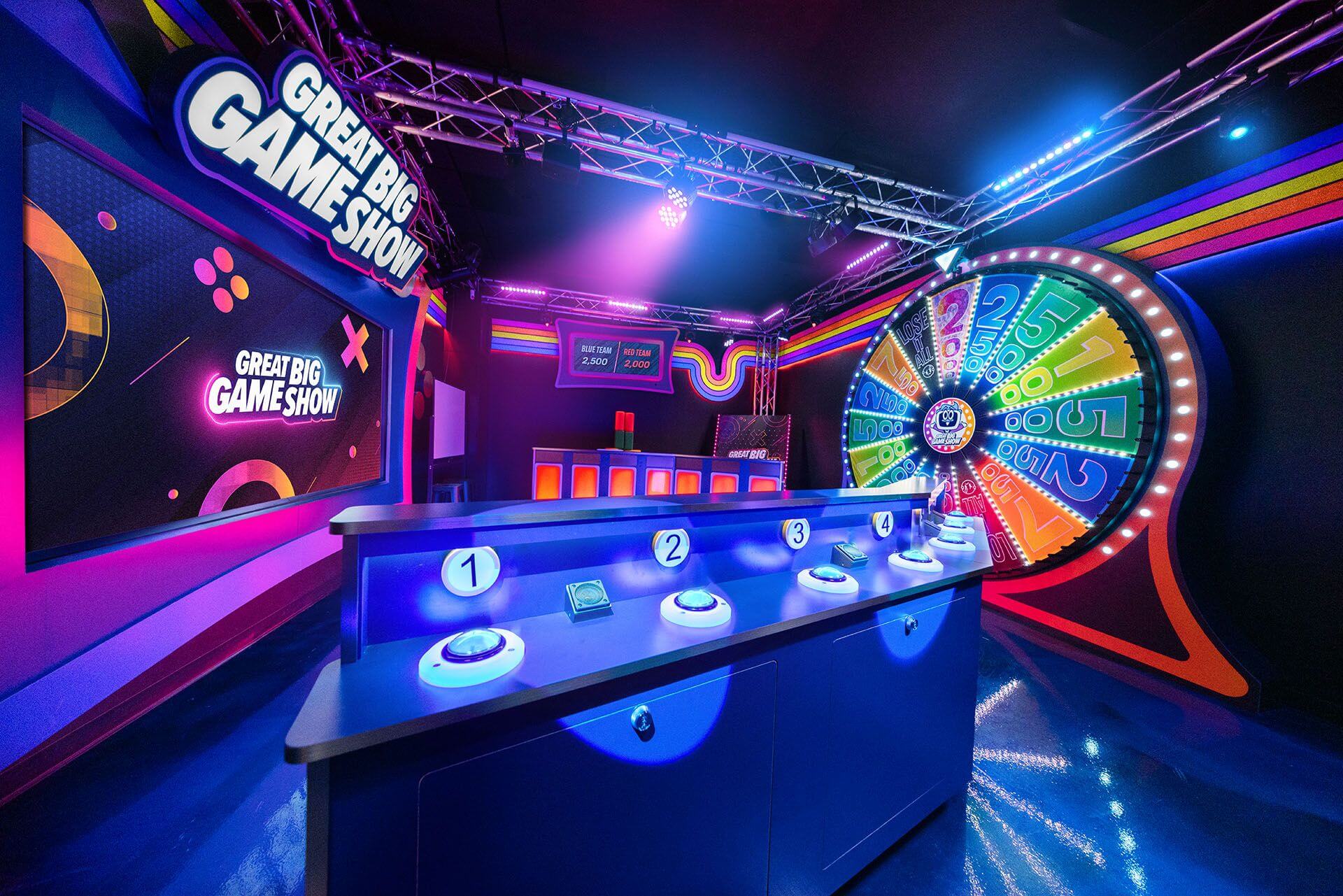 A colorful, neon-lit game show studio with a large prize wheel and contestant podiums in Santa Clara, California.