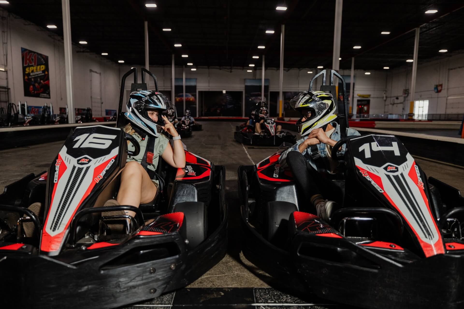 Two people in helmets sitting in go-karts at an indoor racing track in Santa Clara, California.