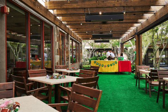 An outdoor patio with wooden tables and chairs on artificial green turf in Santa Clara, California.